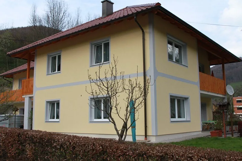 Gelbe Fassade mit grauen Faschen an einem zweistöckigen Wohnhaus