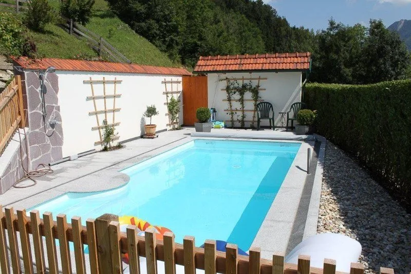 Pool mit heller Steinumrandung, Holzzaun und weißen Gartenhäuschen