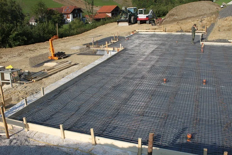 Bewehrte Bodenplatte einer Baustelle am Hang, Bagger im Hintergrund