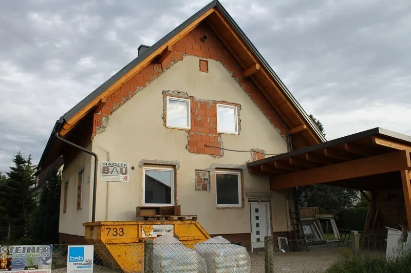 Wohnhaus mit Carport vor der Sanierung, alter Putz teilweise abgeschlagen, Mulde davor