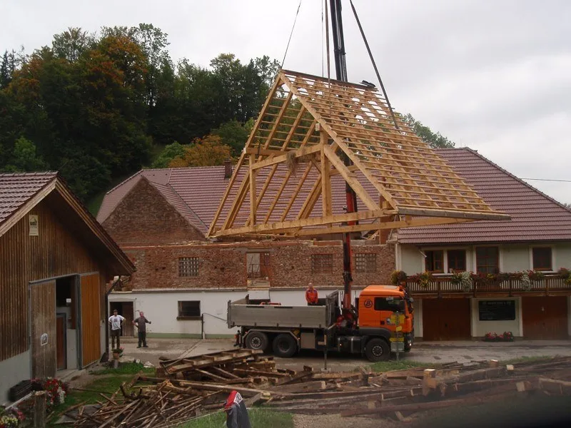 Ein Kran hebt einen neuen Dachstuhl auf ein Bauernhaus
